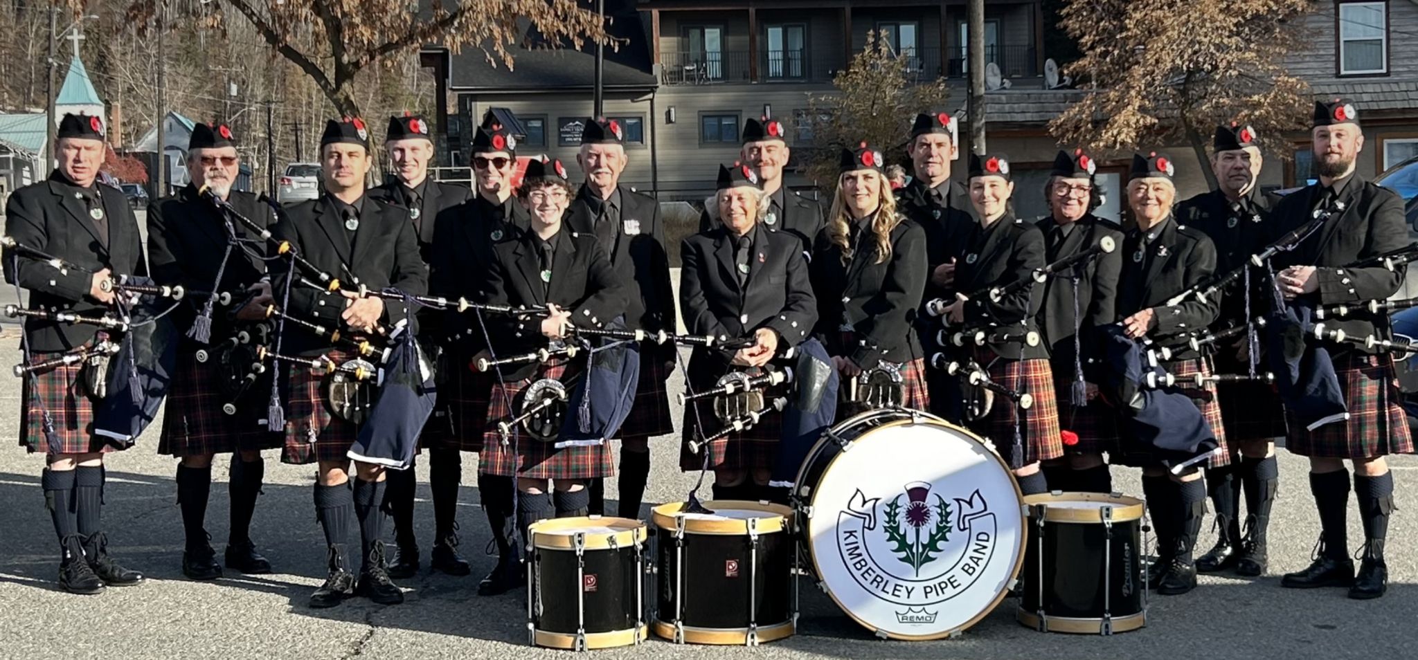 Kimberley Pipe Band members in uniform holding bagpipes, with their bass drum and snare drums in front